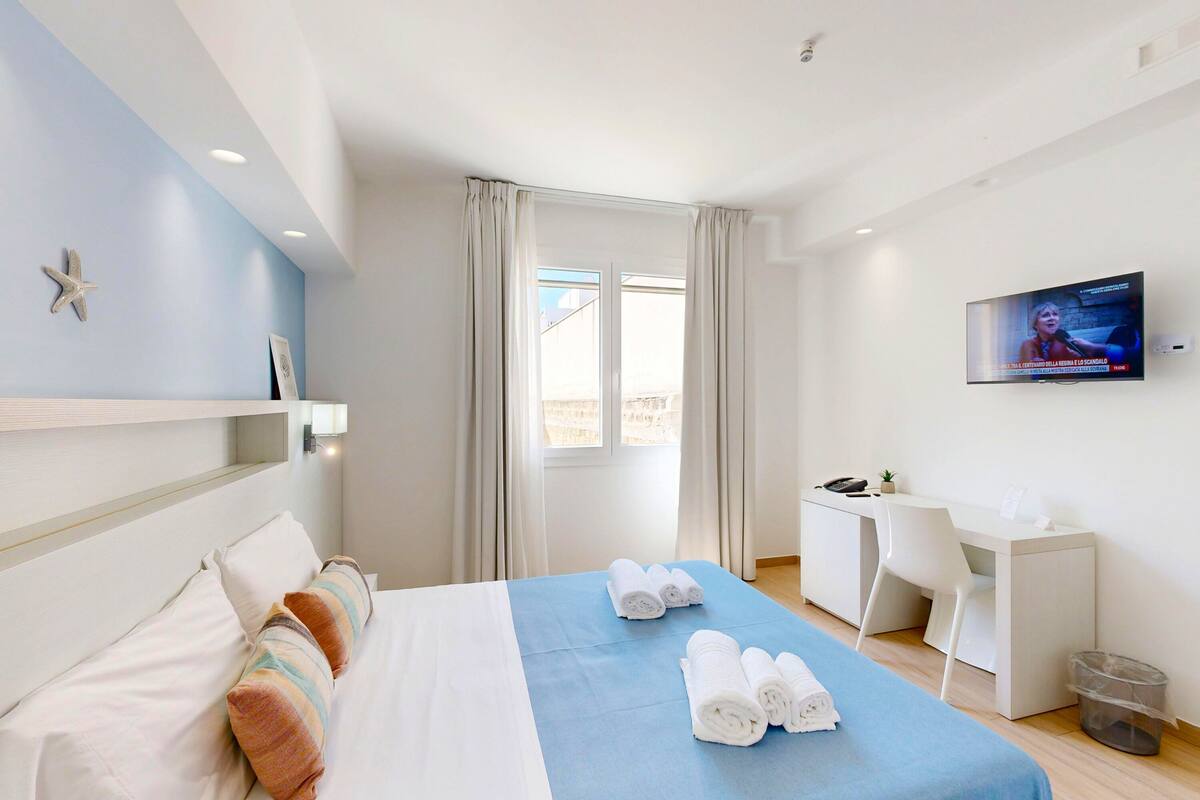 Een hotelkamer met een bed, bureau, televisie en raam met gordijnen.