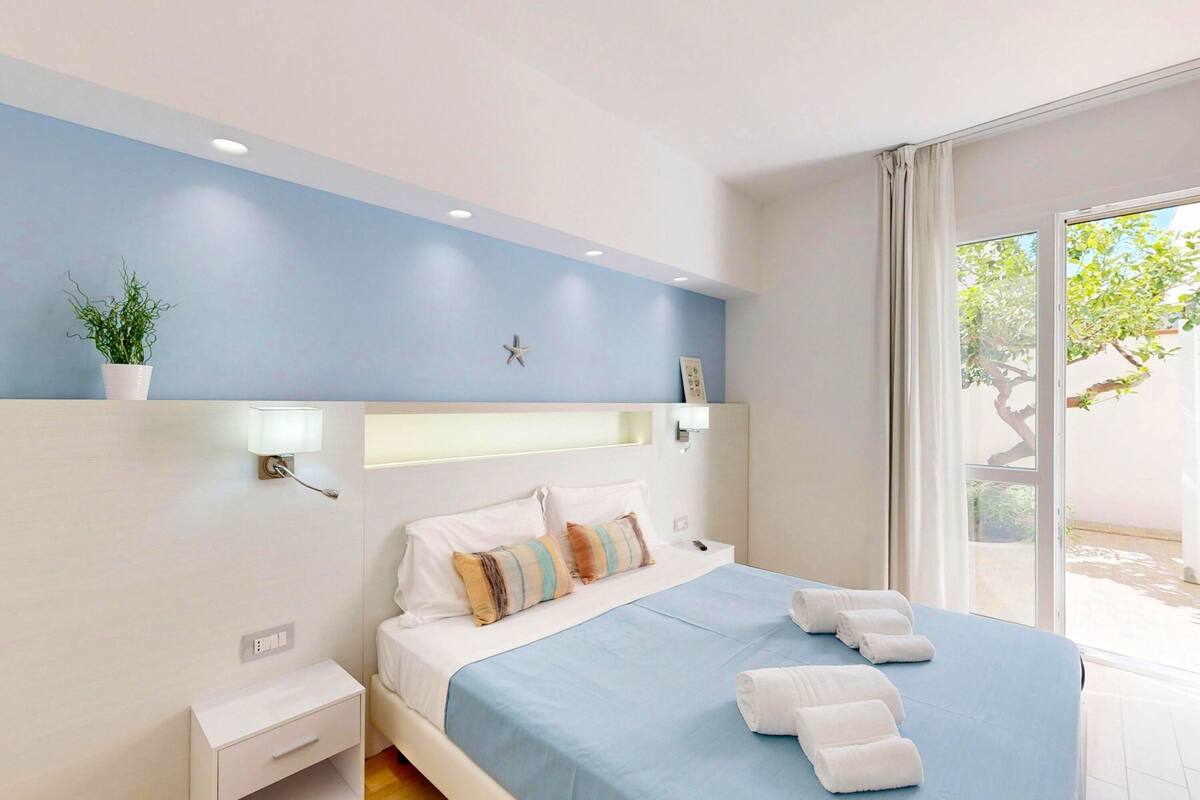 Een moderne slaapkamer met een bed, nachtkastjes, een kamerplant en een raam met uitzicht.