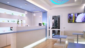 A modern reception area with a counter, seating, and a TV screen. - Hotel Perla Gaia (San Vito Lo Capo)