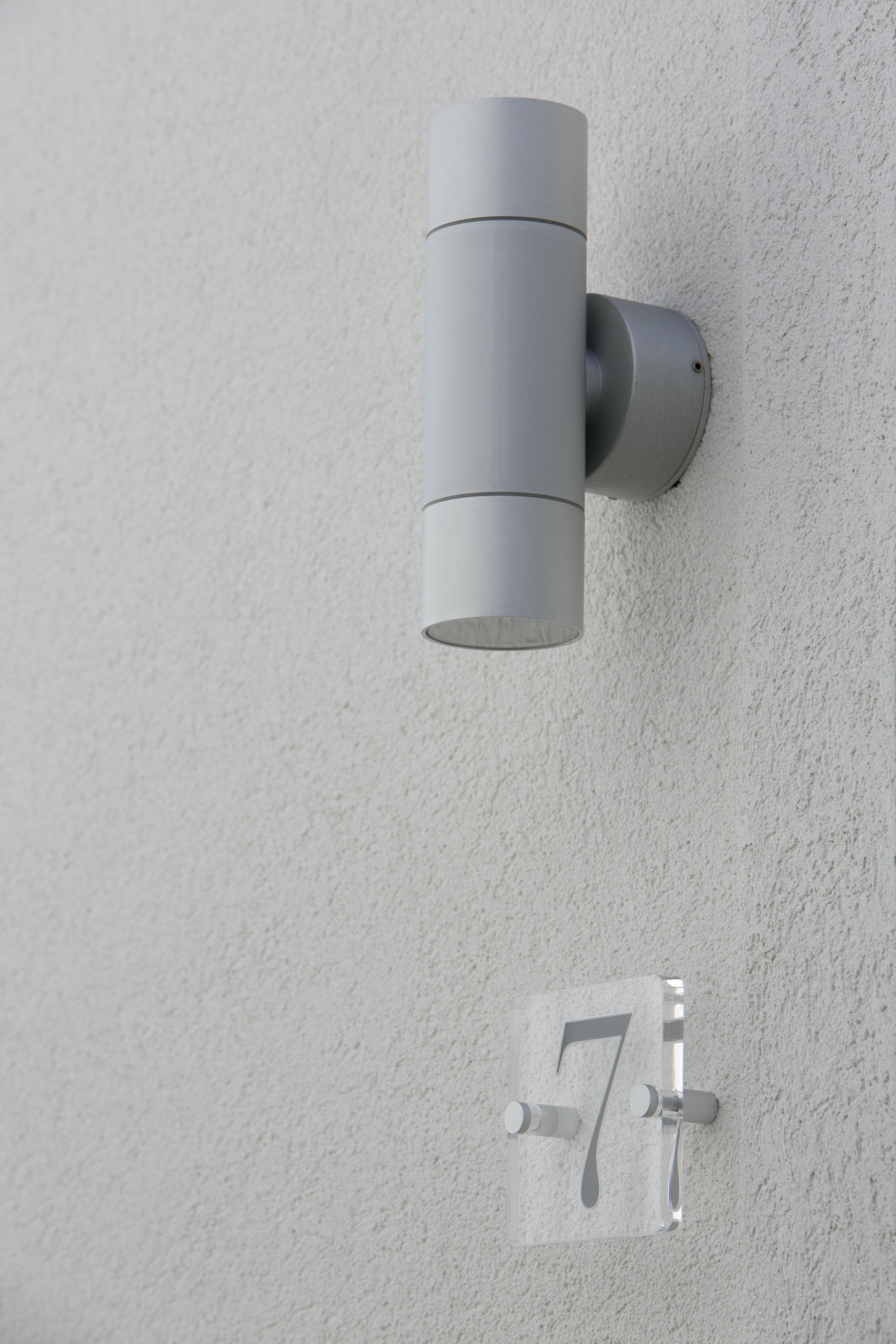 A wall-mounted light fixture with a cylindrical design and a clear number plate indicating room 7.