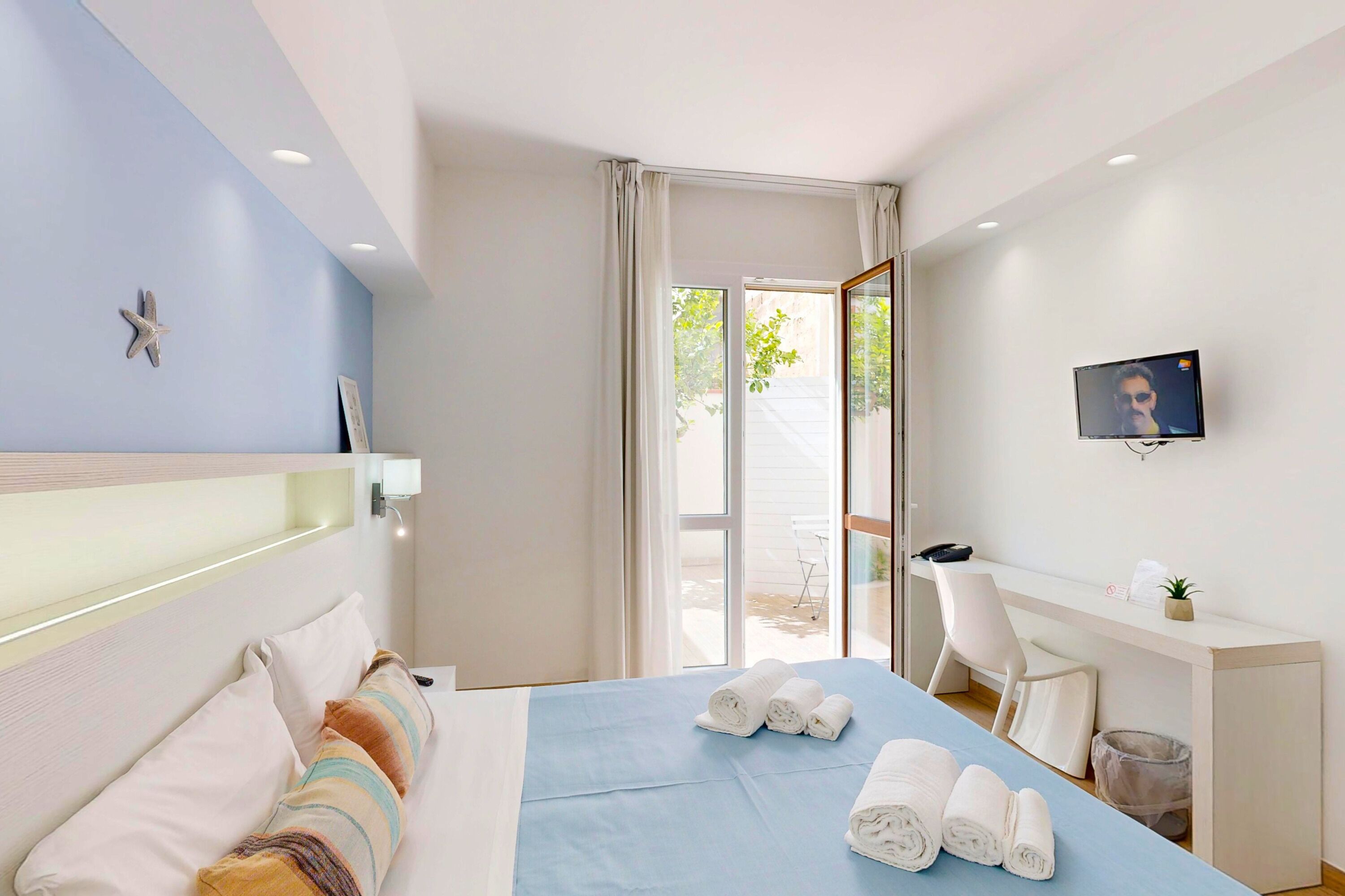 Una habitación de hotel con una cama, un escritorio, un televisor y un balcón.