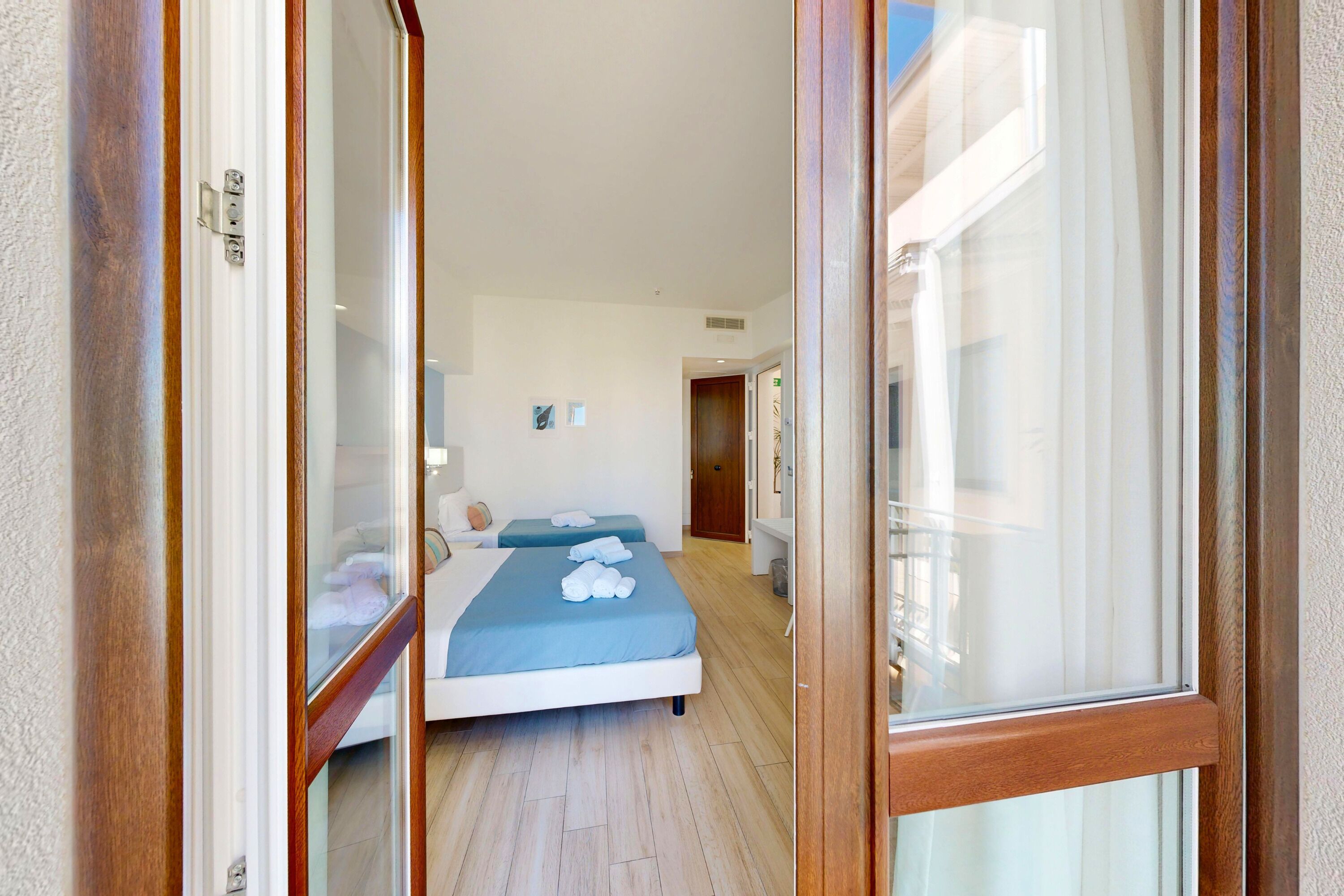 A hotel room with a wooden door, a bed with blue bedding, a bedside table, and a small bedside lamp.