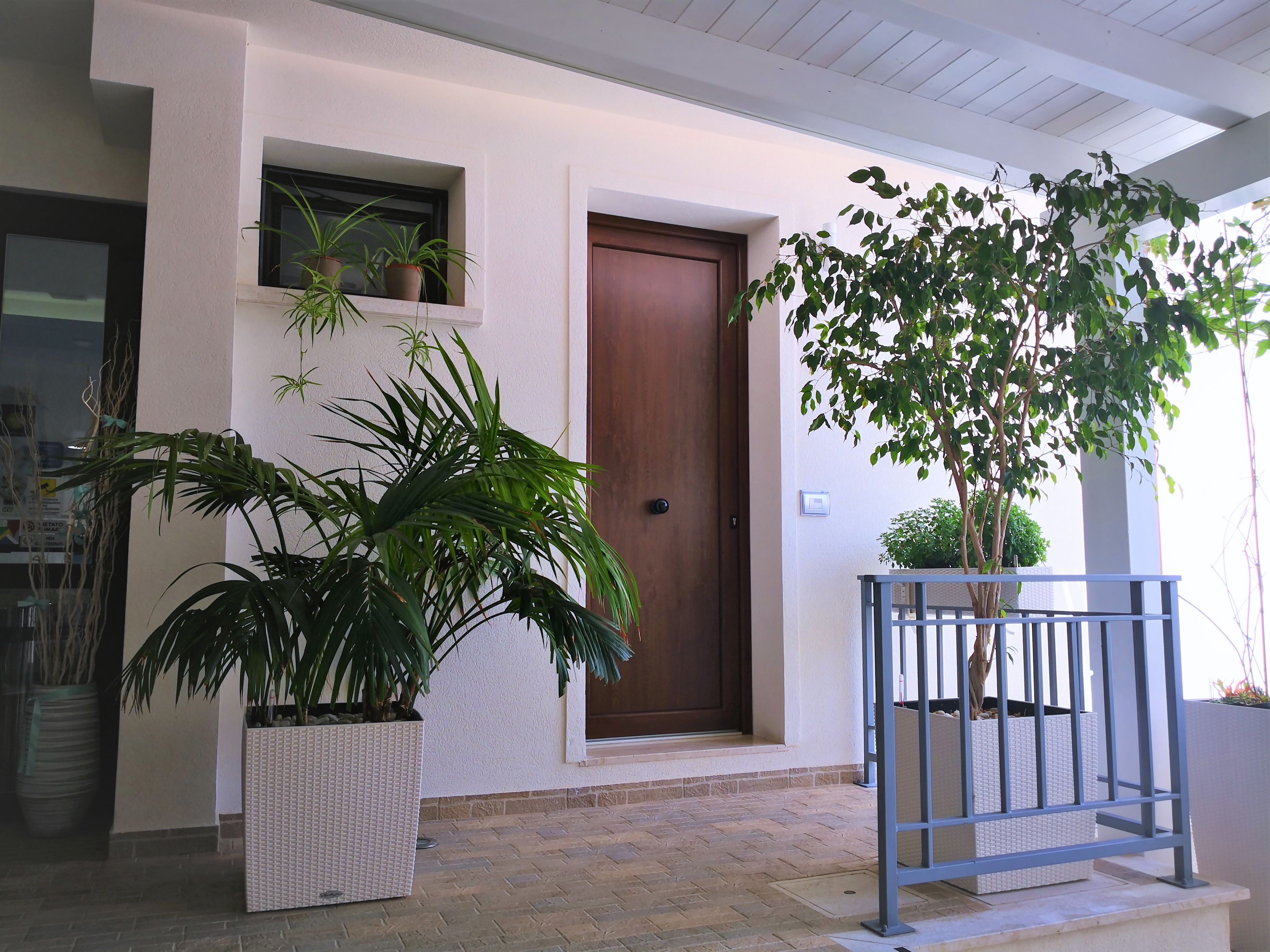 A building entrance with a brown door, potted plants, and a metal railing.