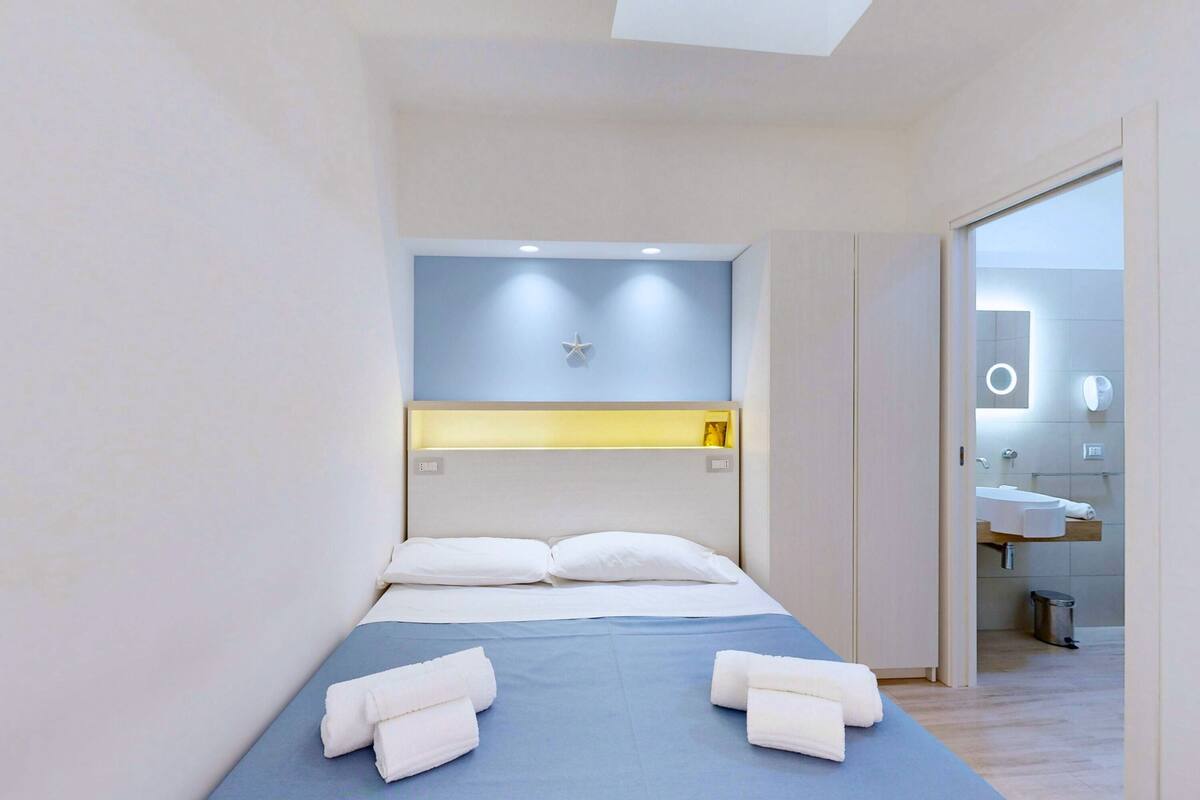 Een moderne hotelkamer met een bed, nachtkastje, wanddecoratie van een ster en een badkamer zichtbaar door een geopende deur.