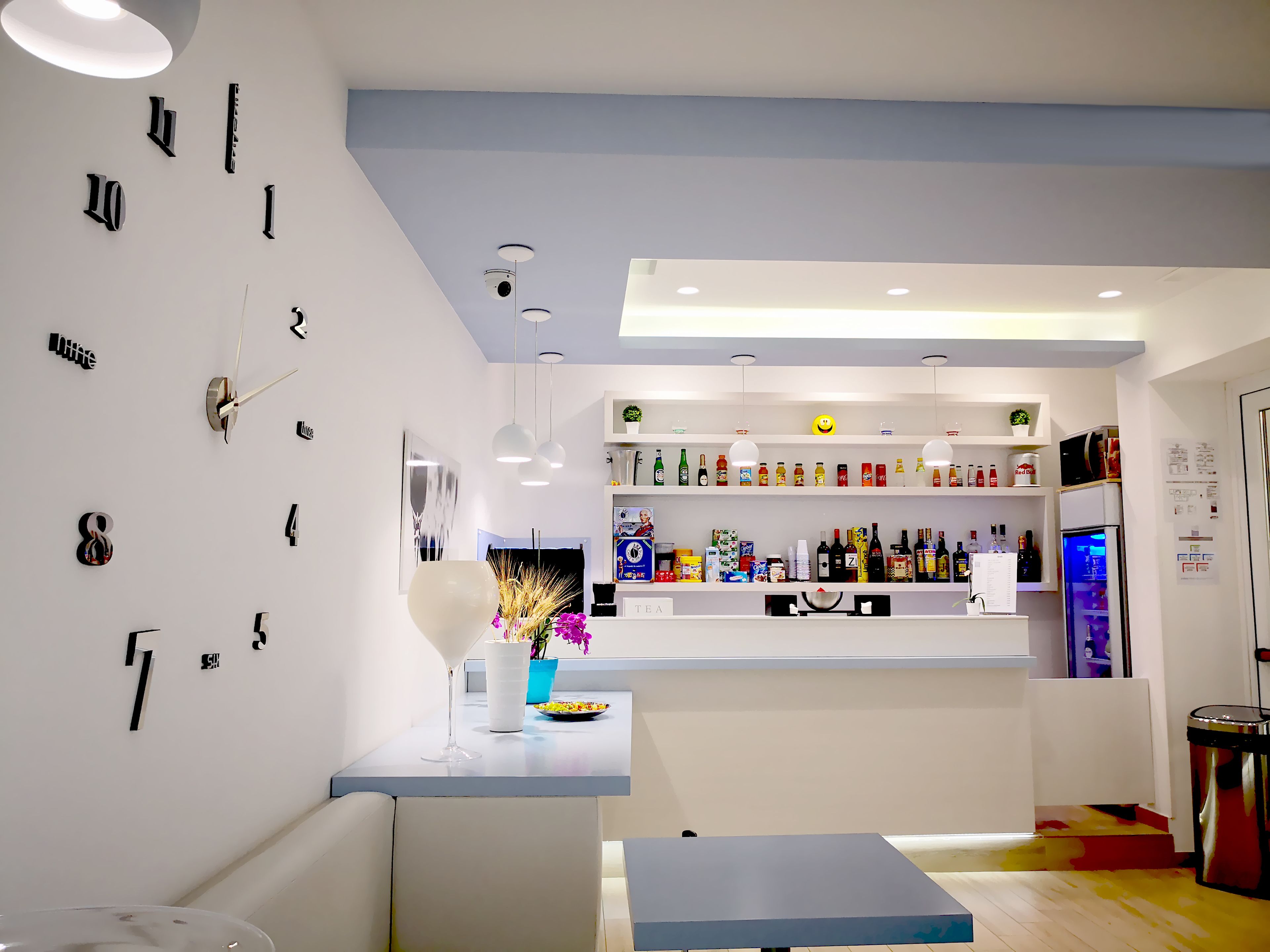 A modern bar area with a white countertop, shelves stocked with beverages, and a clock on the wall.