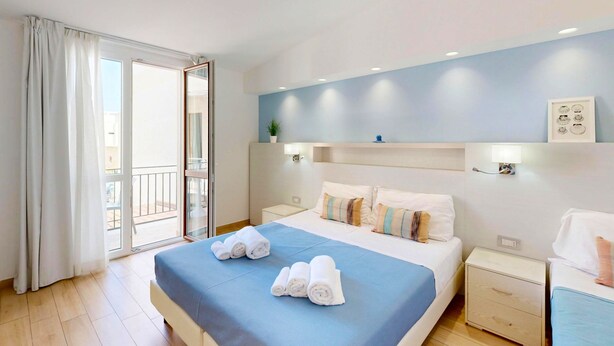 A hotel room with a bed, two bedside tables, a nightstand, a window with curtains, and a balcony. - Hotel Perla Gaia (San Vito Lo Capo)