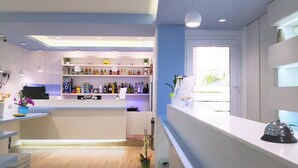 A modern bar area with wooden flooring, white countertops, and shelves stocked with bottles. - Hotel Perla Gaia (San Vito Lo Capo)