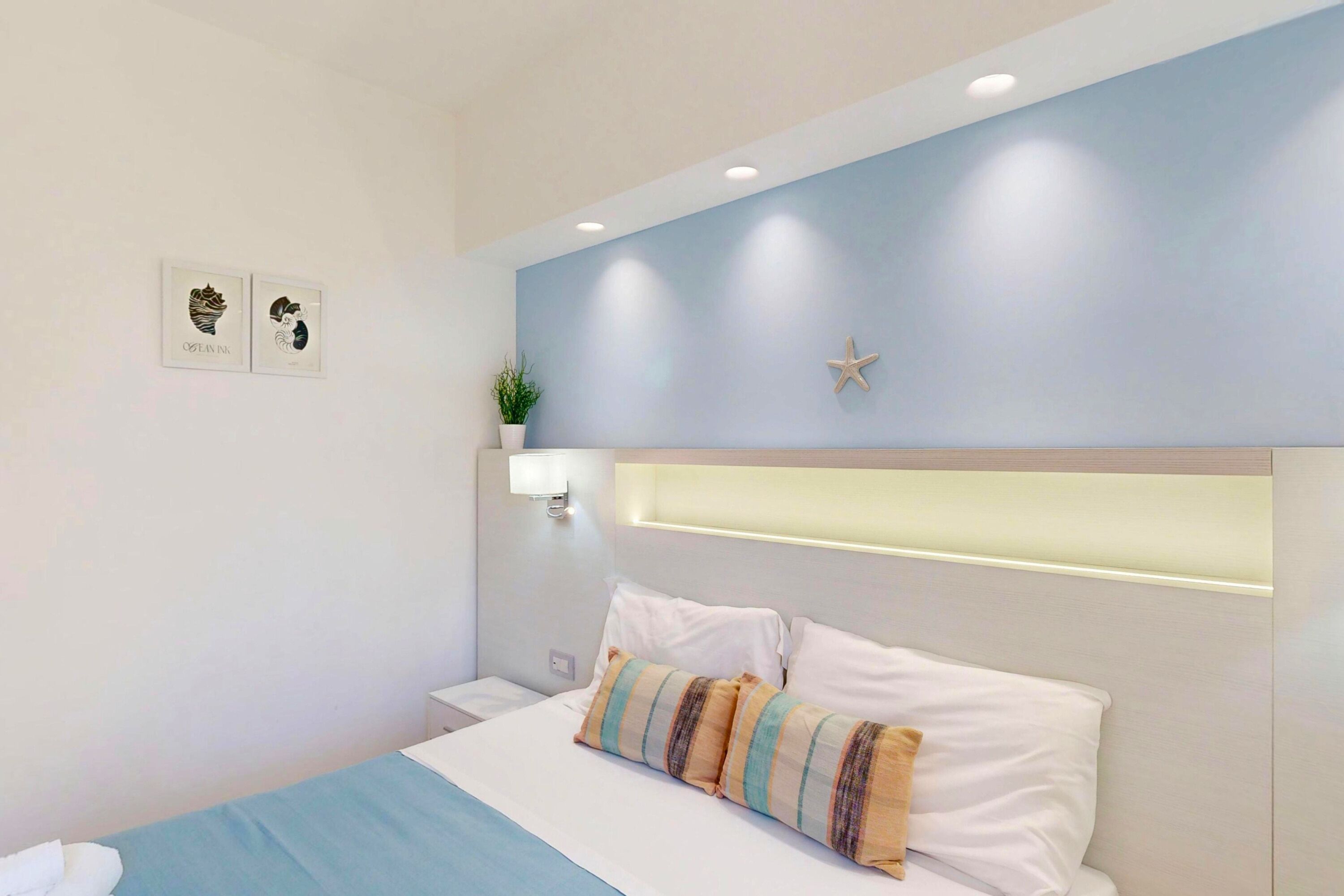 Une chambre à coucher avec un lit, une plante fixée au mur, une décoration en forme d’étoile et deux tableaux encadrés.