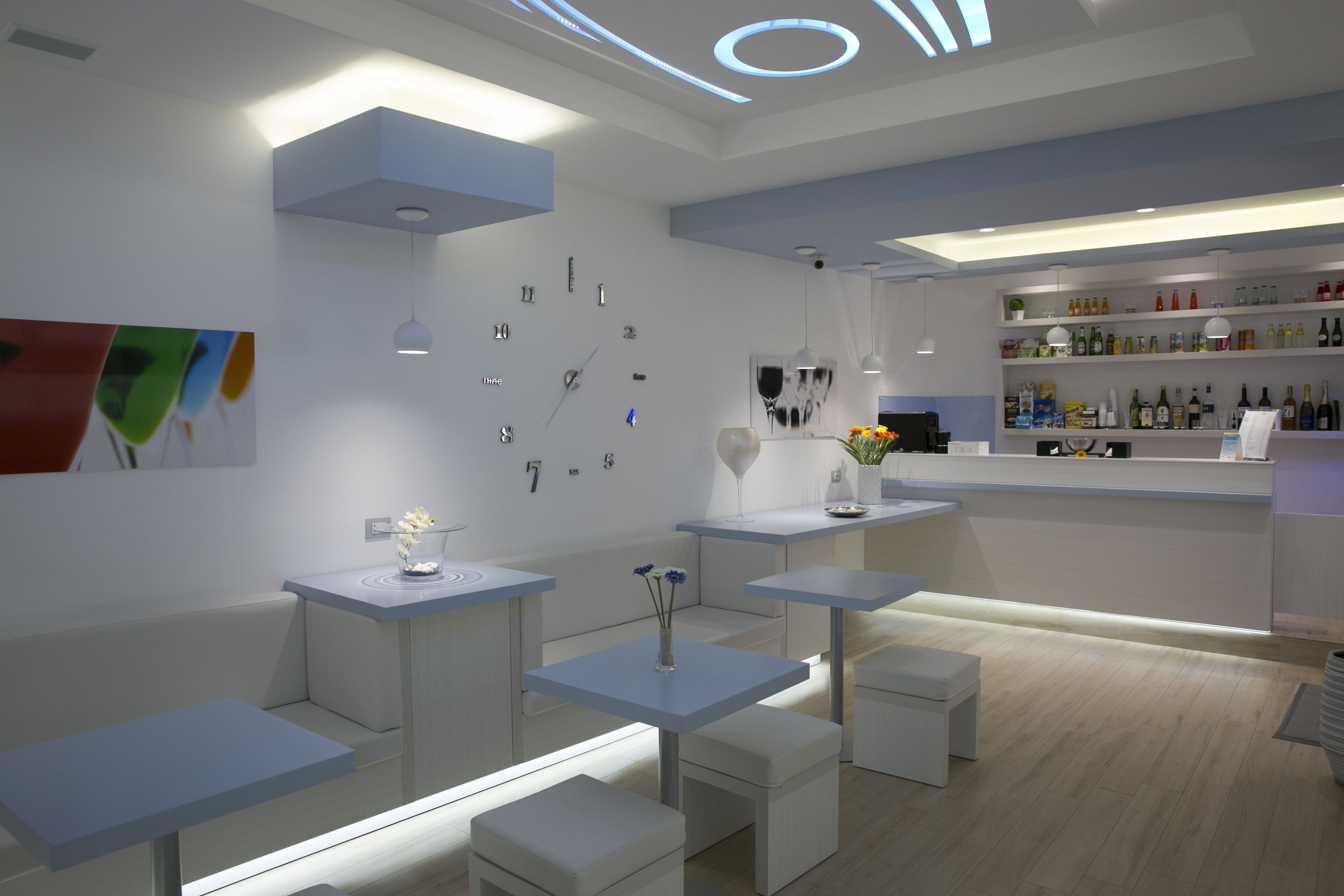 Un área de bar moderna con mobiliario blanco, un reloj en la pared y estantes con botellas.
