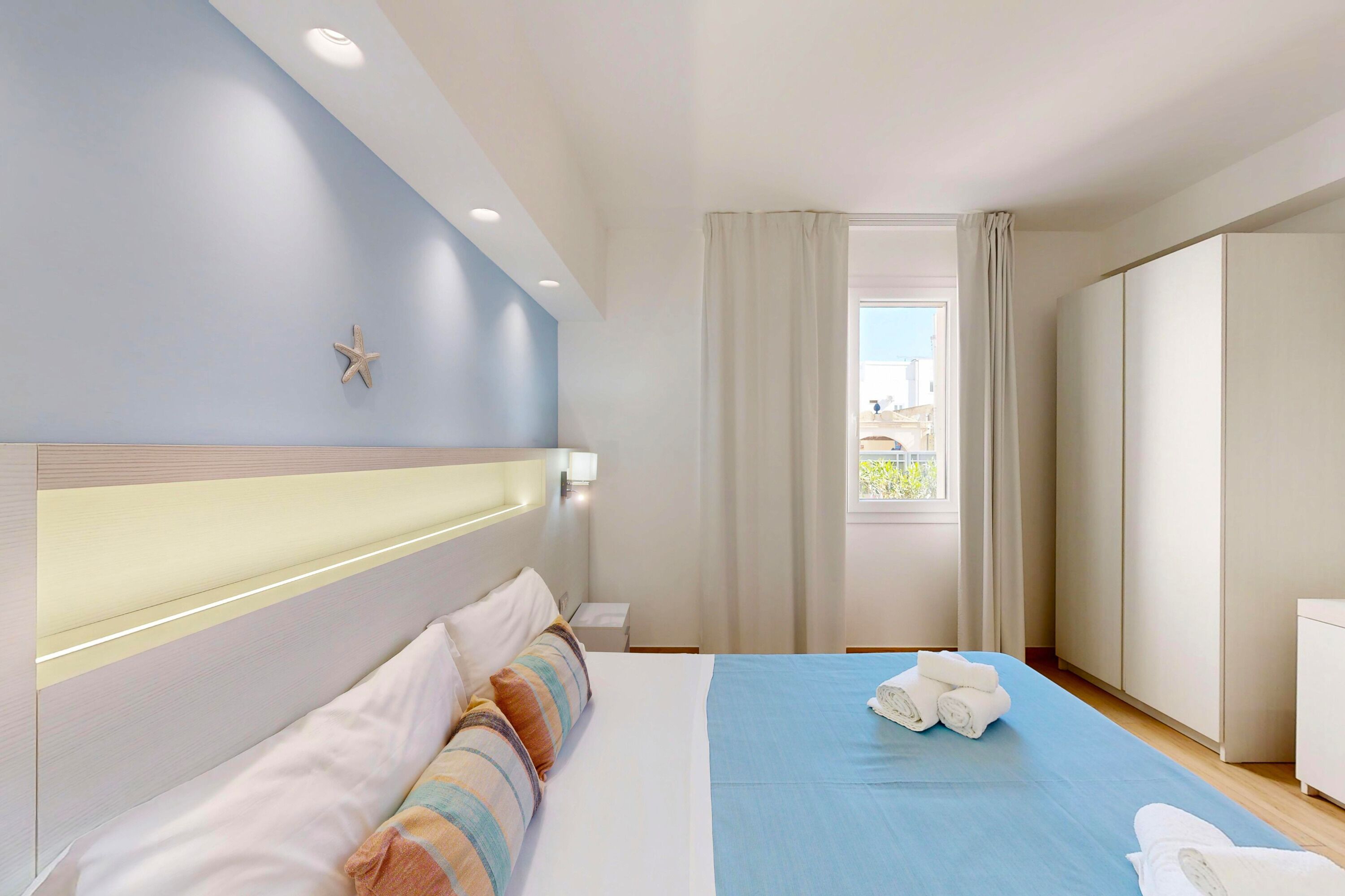 Une chambre d’hôtel avec un lit, une table de chevet, une armoire et une fenêtre avec des rideaux.