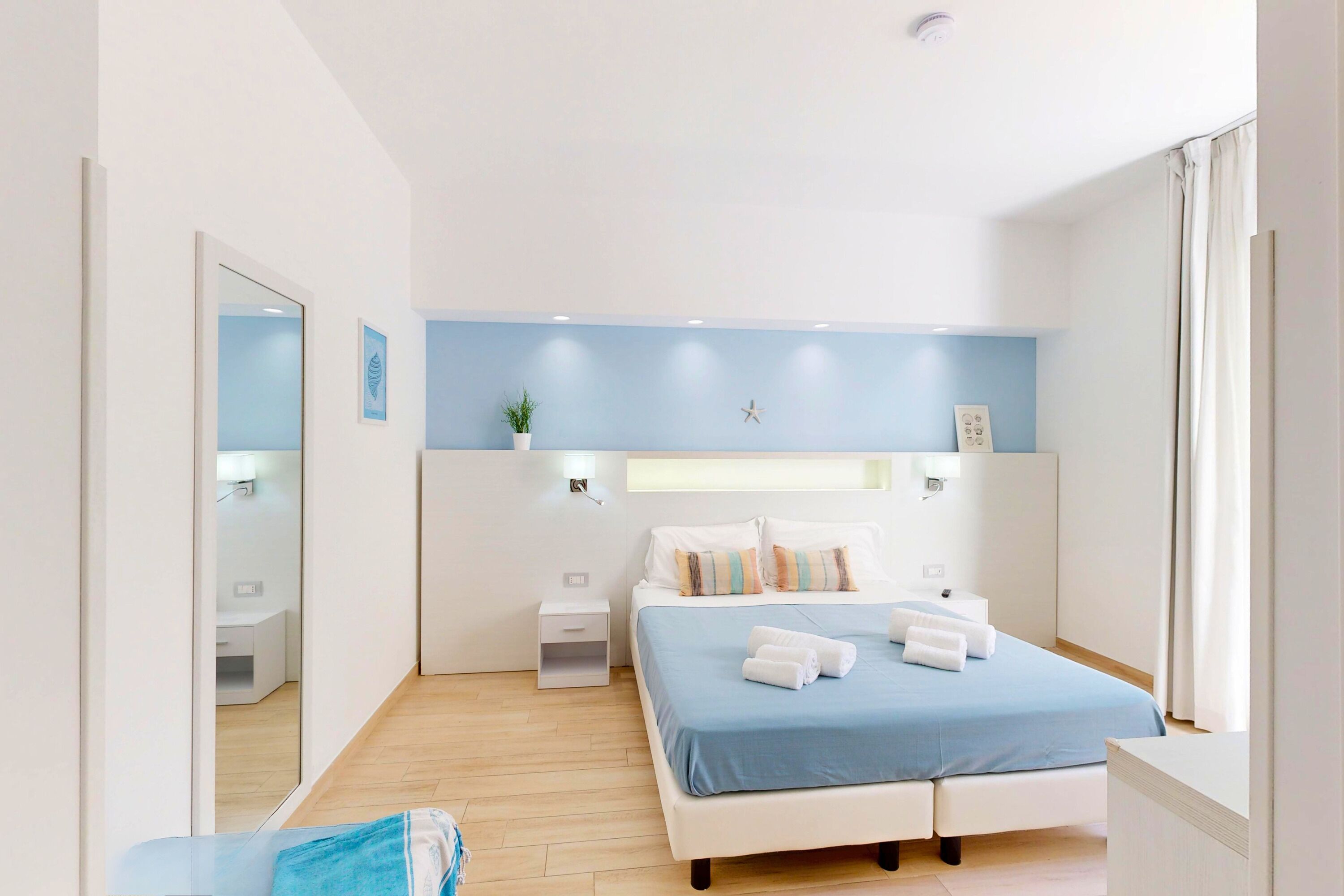 A modern bedroom with a bed, bedside tables, a nightstand, a mirror, and a wall-mounted star decoration.