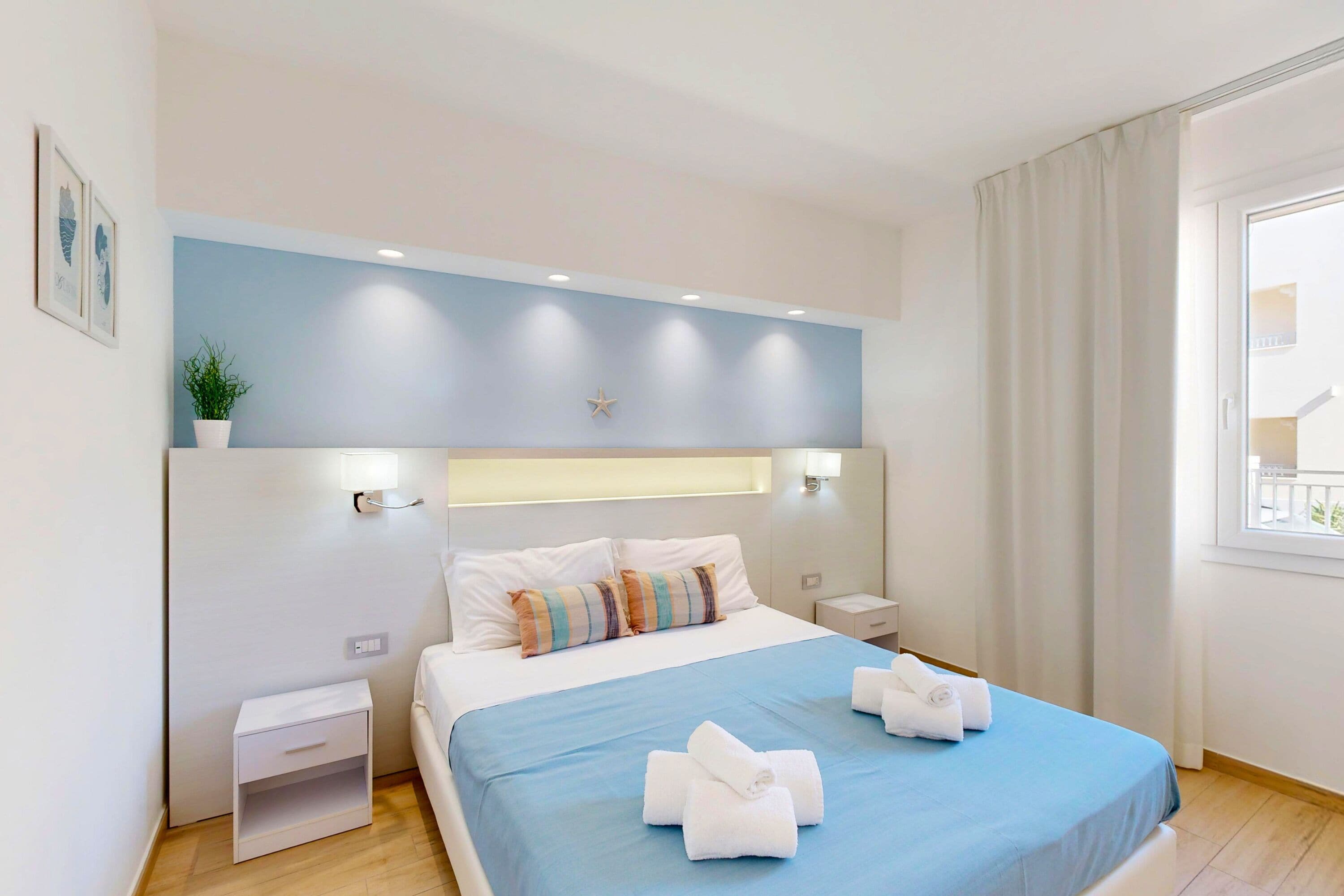 Ein ordentlich eingerichtetes Hotelzimmer mit Bett, Nachttischen, Vorhängen an einem Fenster und einer Stern-Dekoration an der Wand.