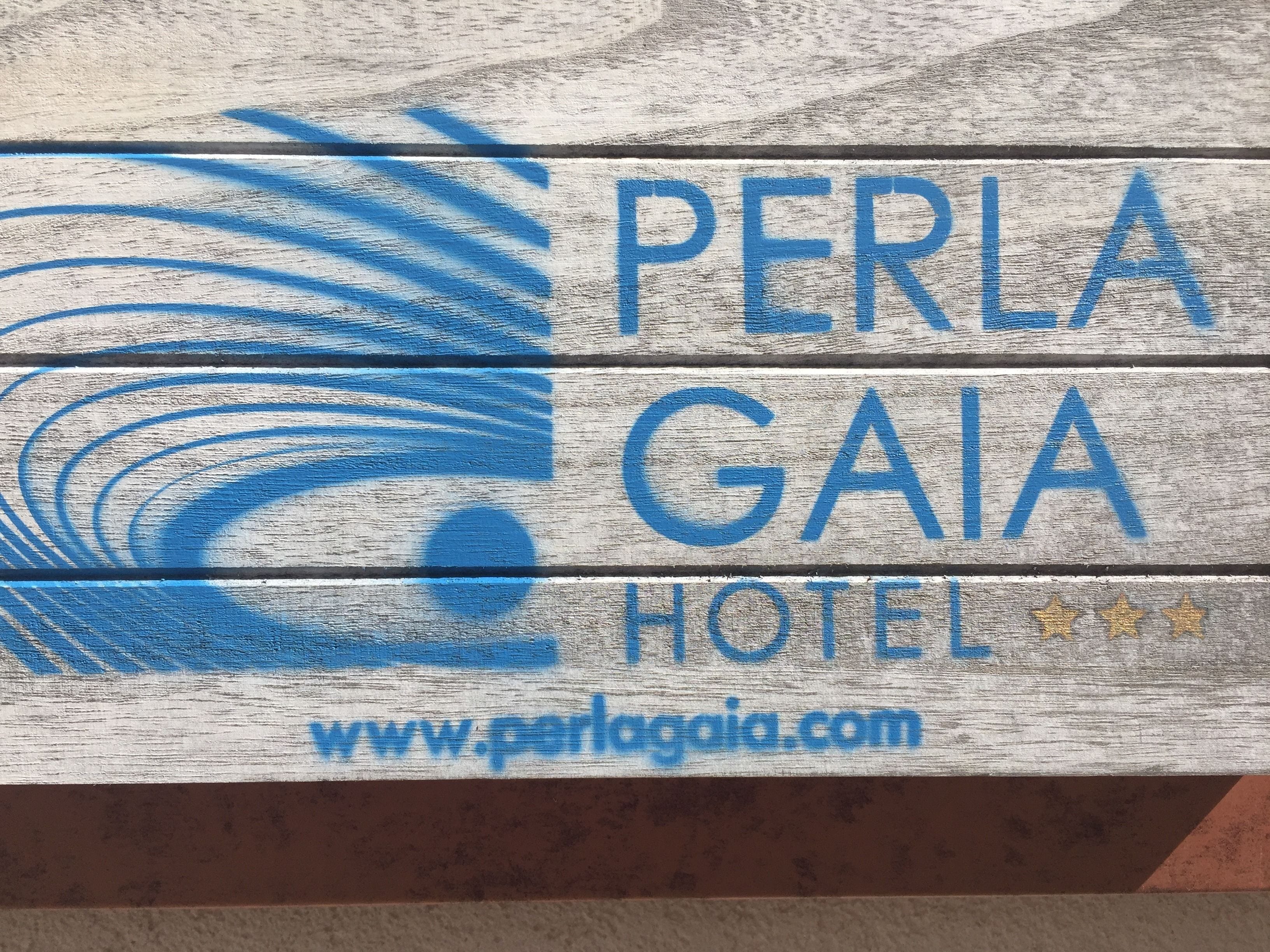 Ein Holzschild mit dem Text "PERLA GAIA HOTEL" und der Internetadresse "www.perlagia.com".