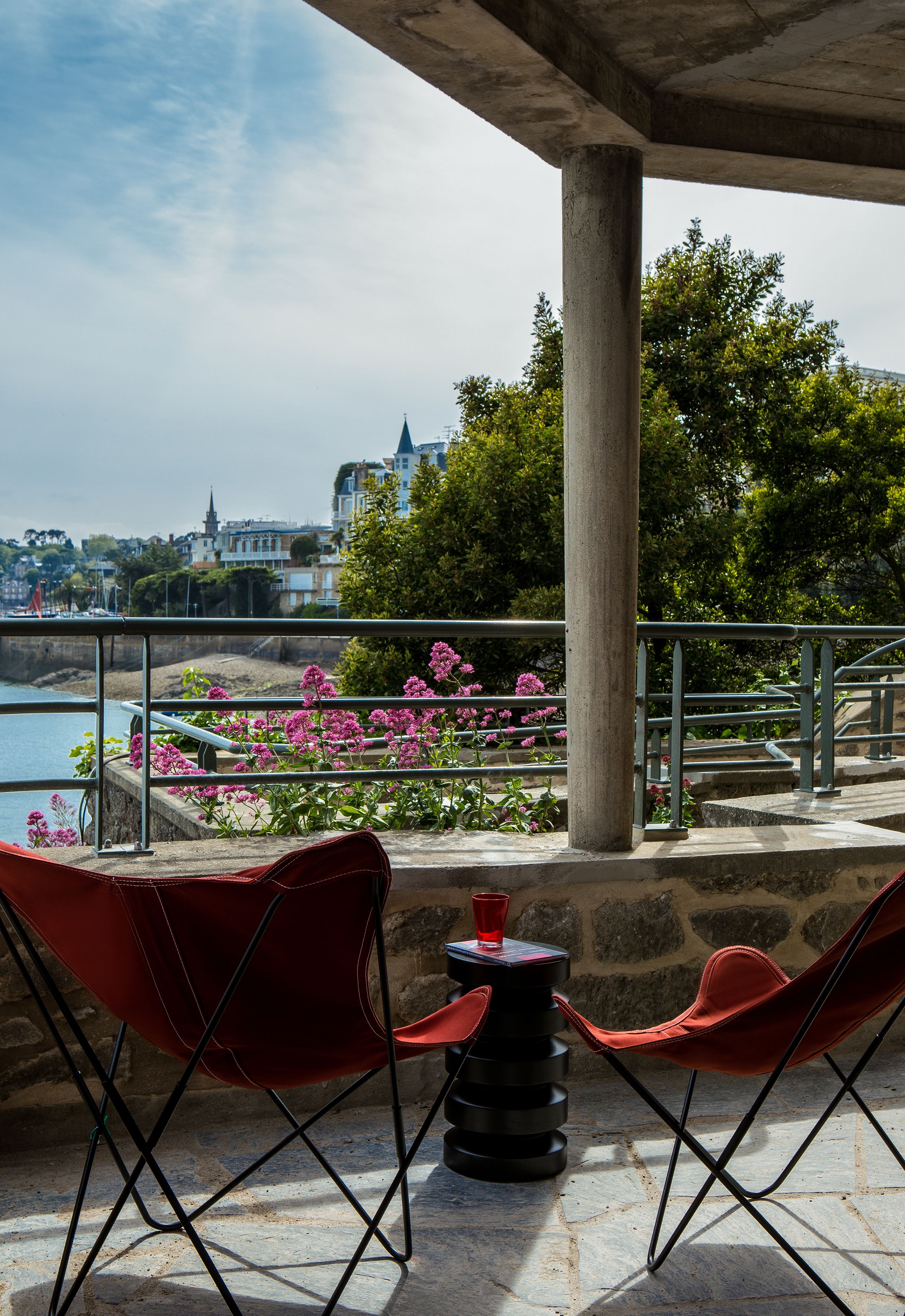 Een terras met rode stoelen en een tafel, met uitzicht op een waterpartij en een stadsbeeld.