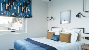 Un dormitorio con cama, ventana, lámpara de pared y un cuadro.