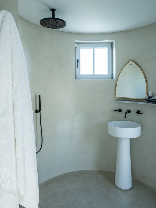 Un baño con lavamanos blanco, cabezal de ducha, toalla y ventana.