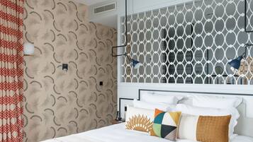 A neatly made bed with white linens and multiple pillows, a patterned wall, and a white headboard with a geometric design.