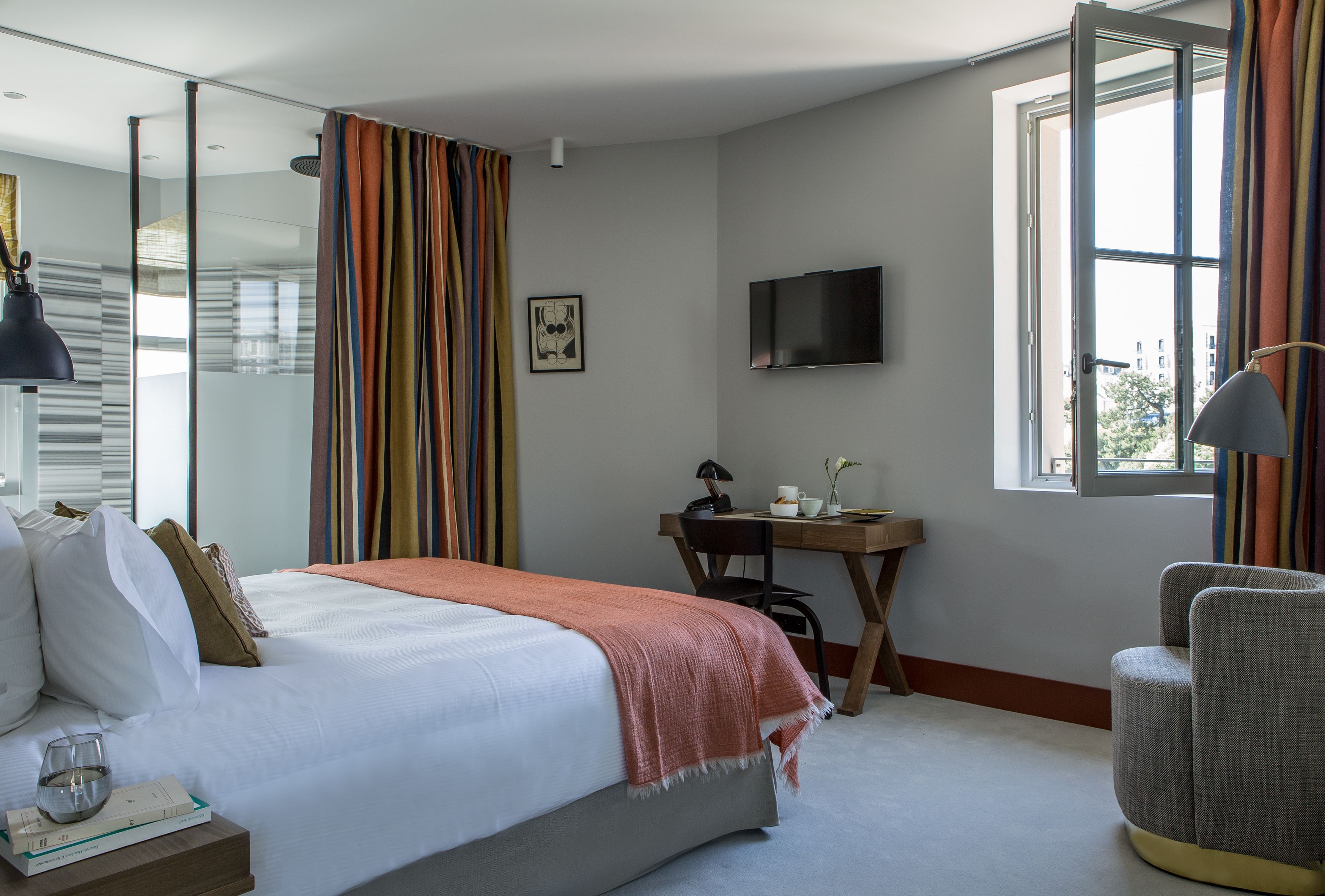 Quarto com uma cama, escrivaninha, cadeira, televisão e janela.