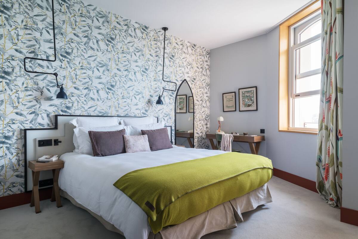 Un dormitorio ordenado con una cama grande, una mesita de noche, un aparador y una ventana con cortinas.
