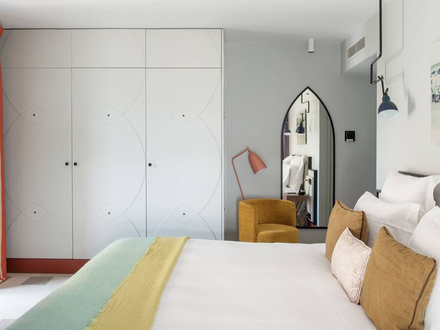A hotel room with a large bed, a wardrobe, a mirror, and a desk with a lamp.