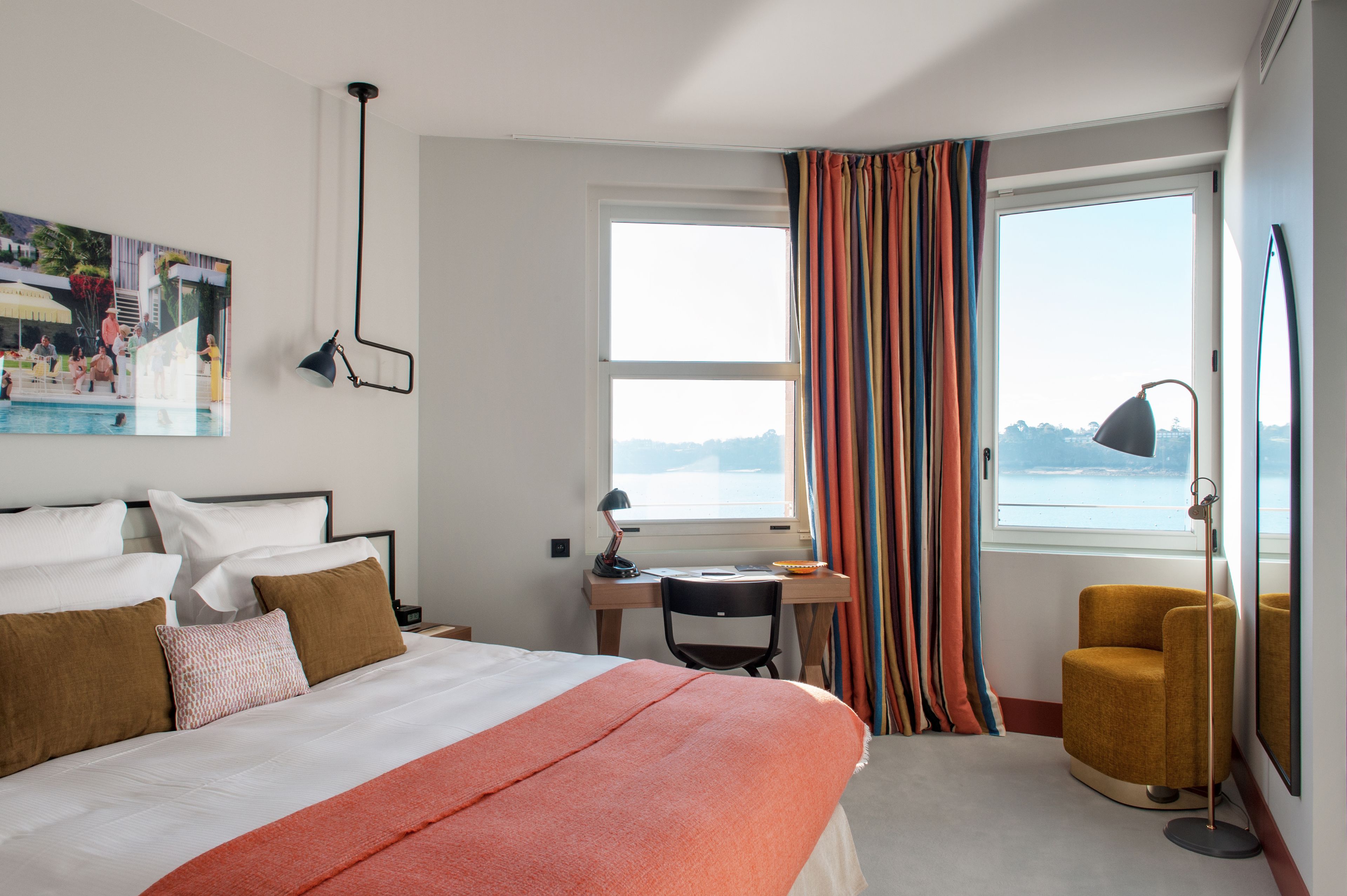 Ein Hotelzimmer mit Bett, Schreibtisch, Stuhl und einem großen Fenster mit Vorhängen.