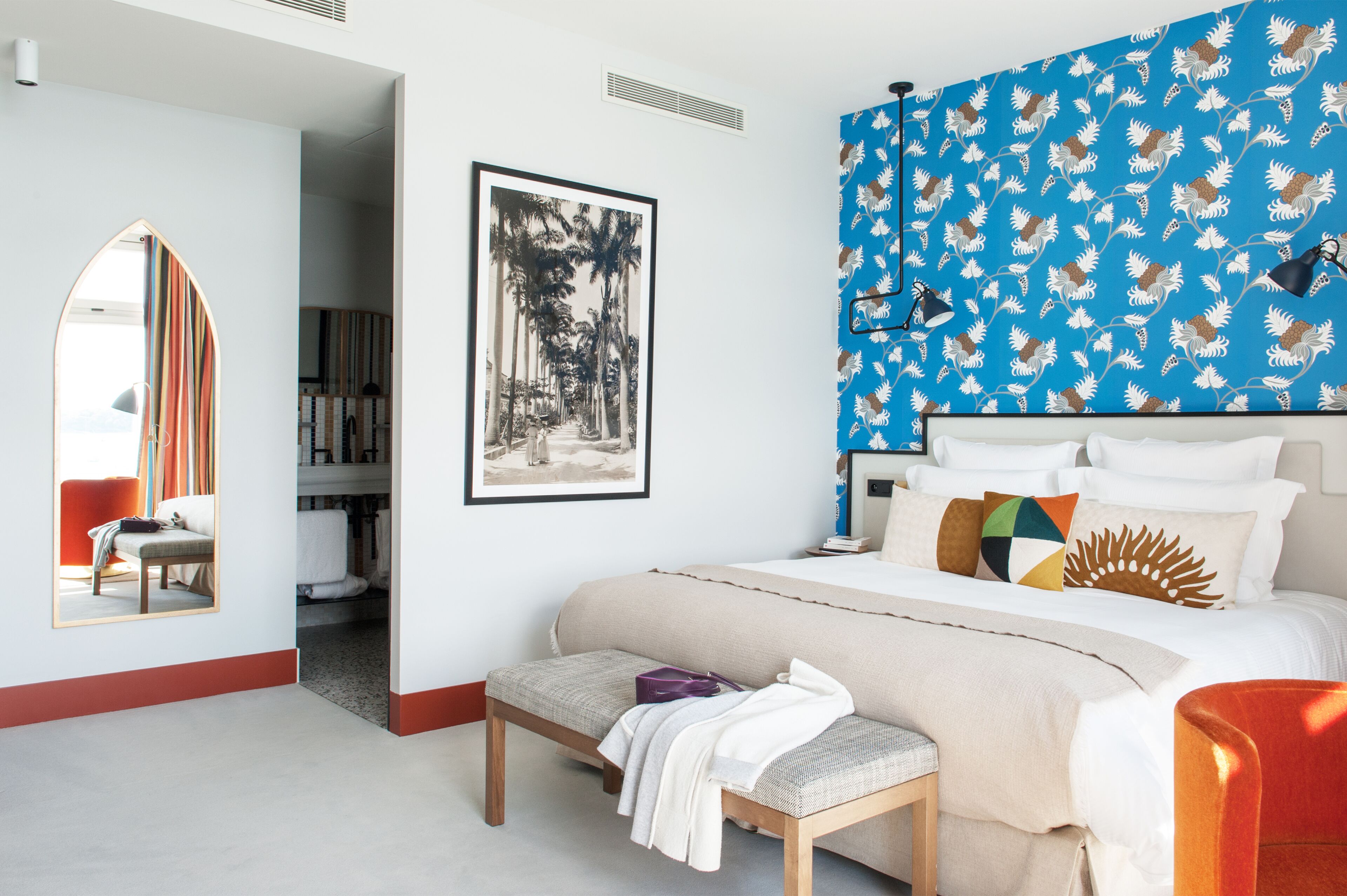 Ein Schlafzimmer mit einem großen Bett, einer Sitzbank, einem Spiegel und einem gerahmten Bild an der Wand.