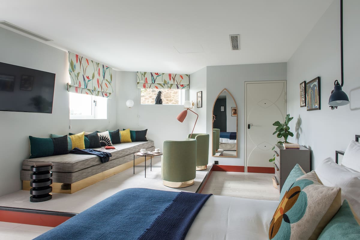 Una habitación de hotel moderna con cama, sofá, sillón, mesita y espejo.