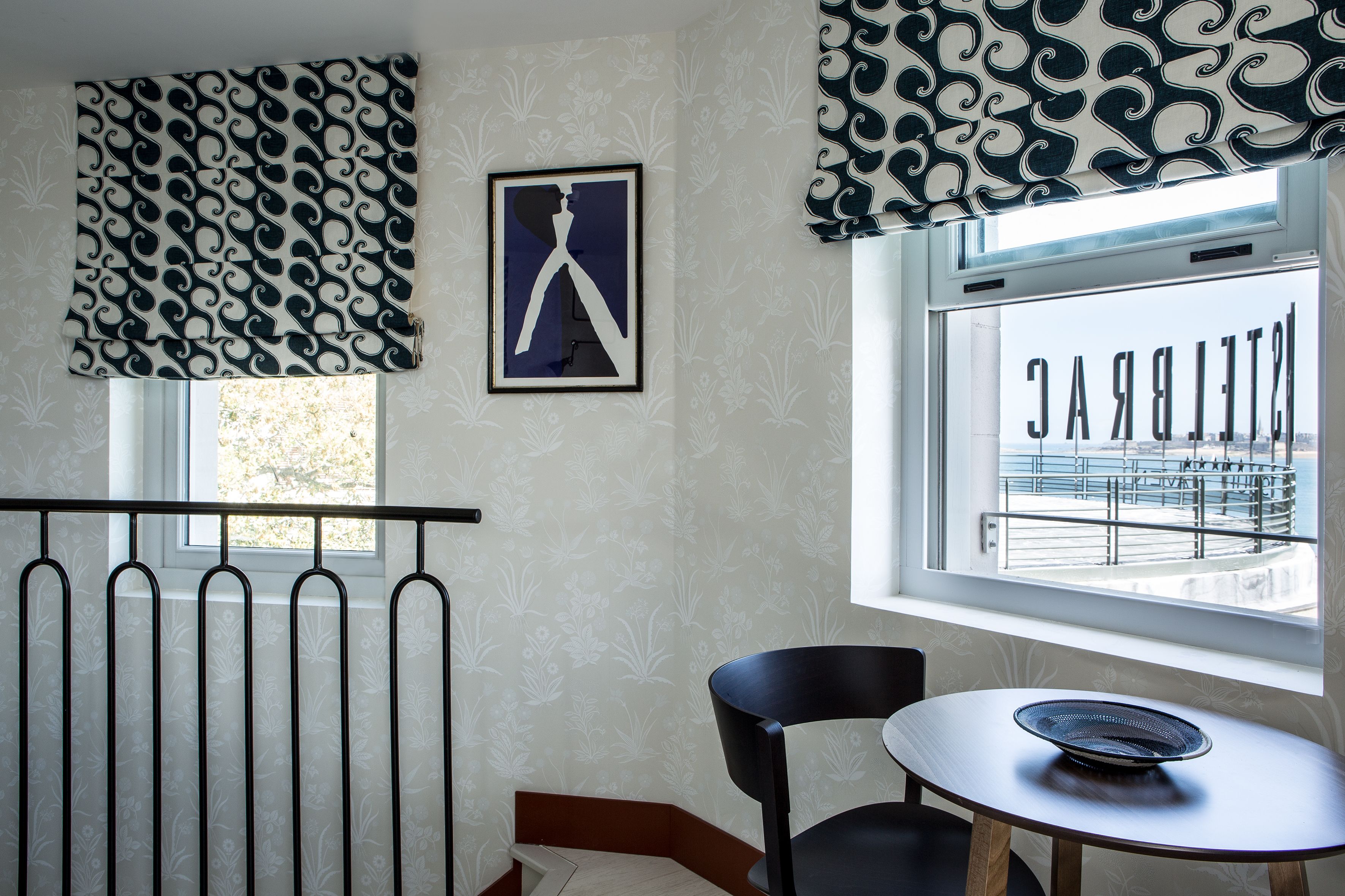 A room with a radiator, a framed picture, a window with a view of a balcony, and a table with a bowl.