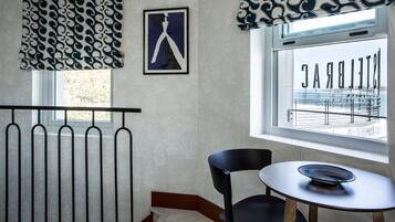 A room with a radiator, a framed picture, a window with a view of a balcony, and a table with a bowl.