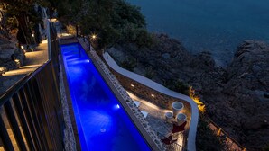 A long, narrow swimming pool with blue lighting, surrounded by stone walls and a railing, overlooking a marina with numerous boats. - Castelbrac Hôtel & Spa (Dinard)