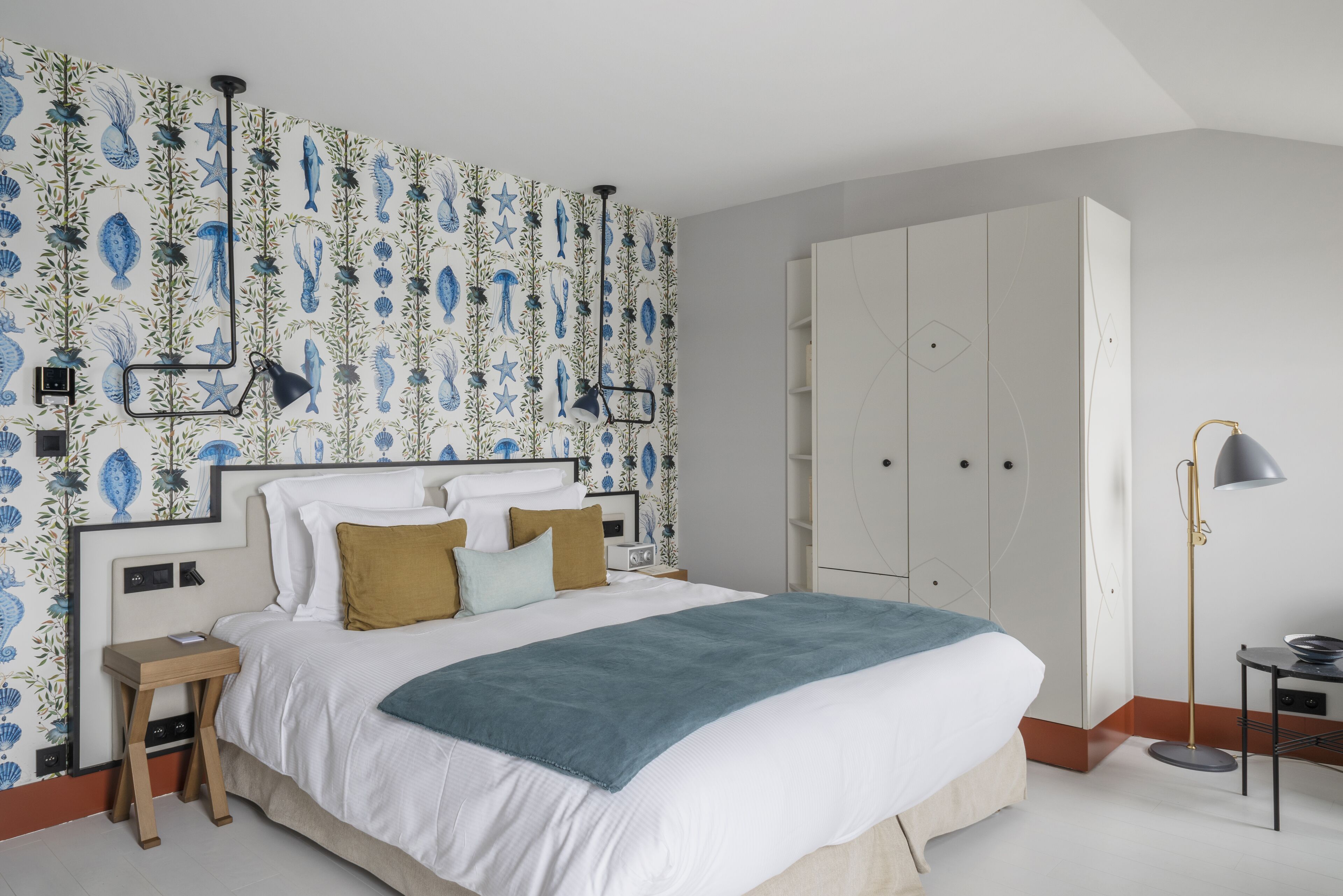 A bedroom with a large bed, a nightstand, a wardrobe, and a wall with a blue and white pattern.