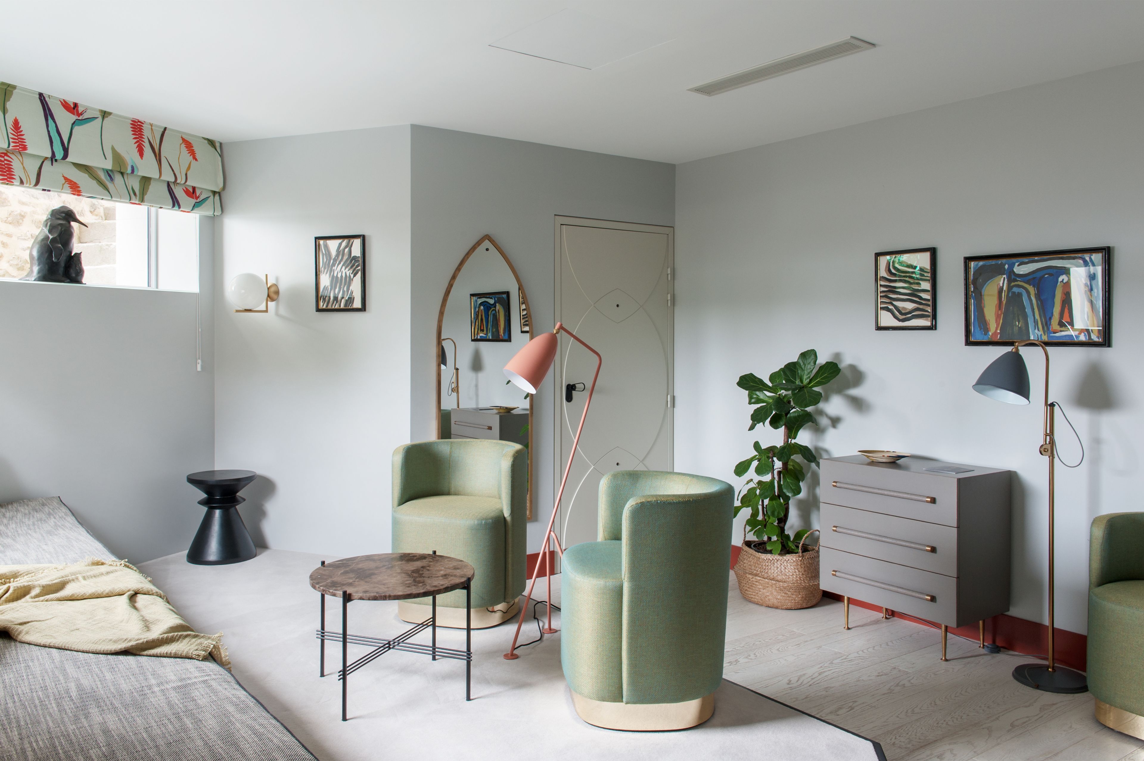 Une chambre moderne comprenant un lit, deux fauteuils, une petite table, une lampe sur pied, une commode et une plante en pot.