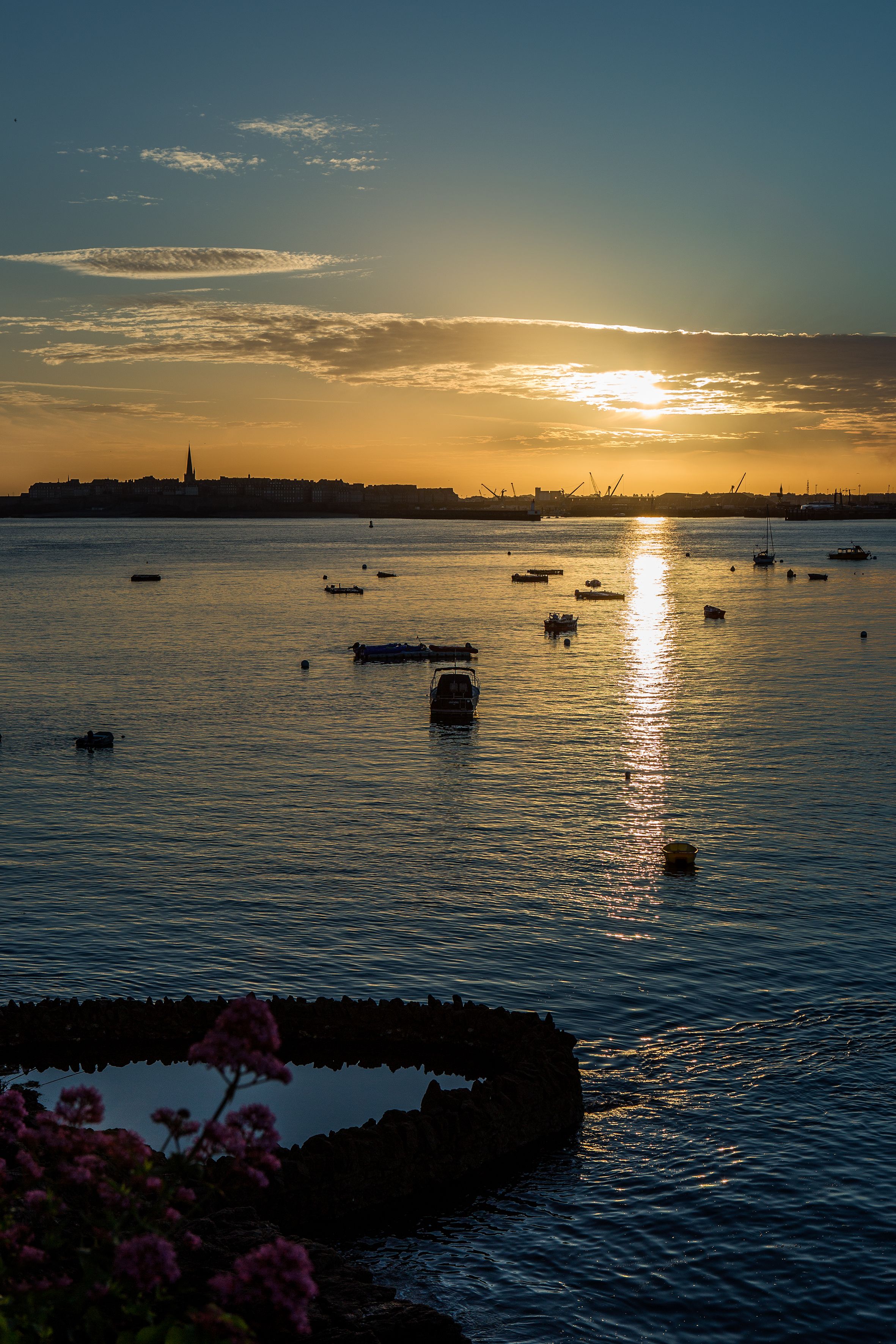 A sunset over a calm body of water with boats and a distant city skyline.