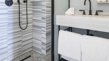 Une salle de bain moderne équipée d’une douche, d’un meuble-lavabo avec miroir et d’un porte-serviettes.
