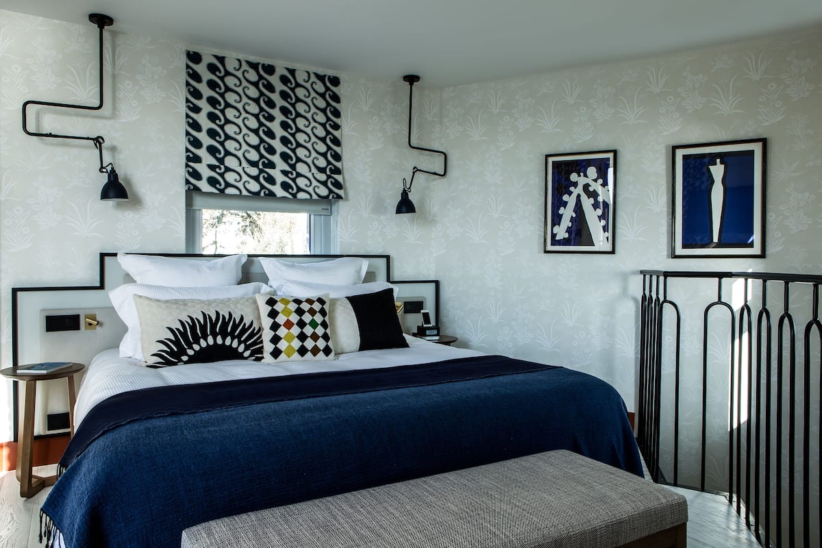 Un dormitorio con una cama grande, dos mesitas de noche, un ventanal con cortinas estampadas y dos lámparas de pared.
