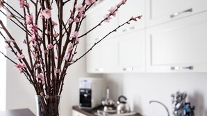 A kitchen with white cabinets, a coffee machine, and a vase with branches and pink flowers. - Rest Guesthouse (Rome)