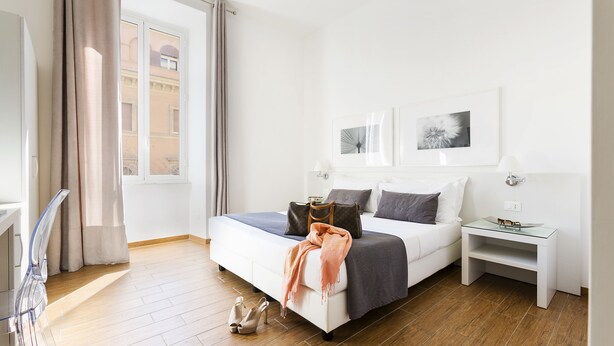 A modern hotel room with a large bed, a bedside table, and a view of the city through the window. - Rest Guesthouse (Rome)