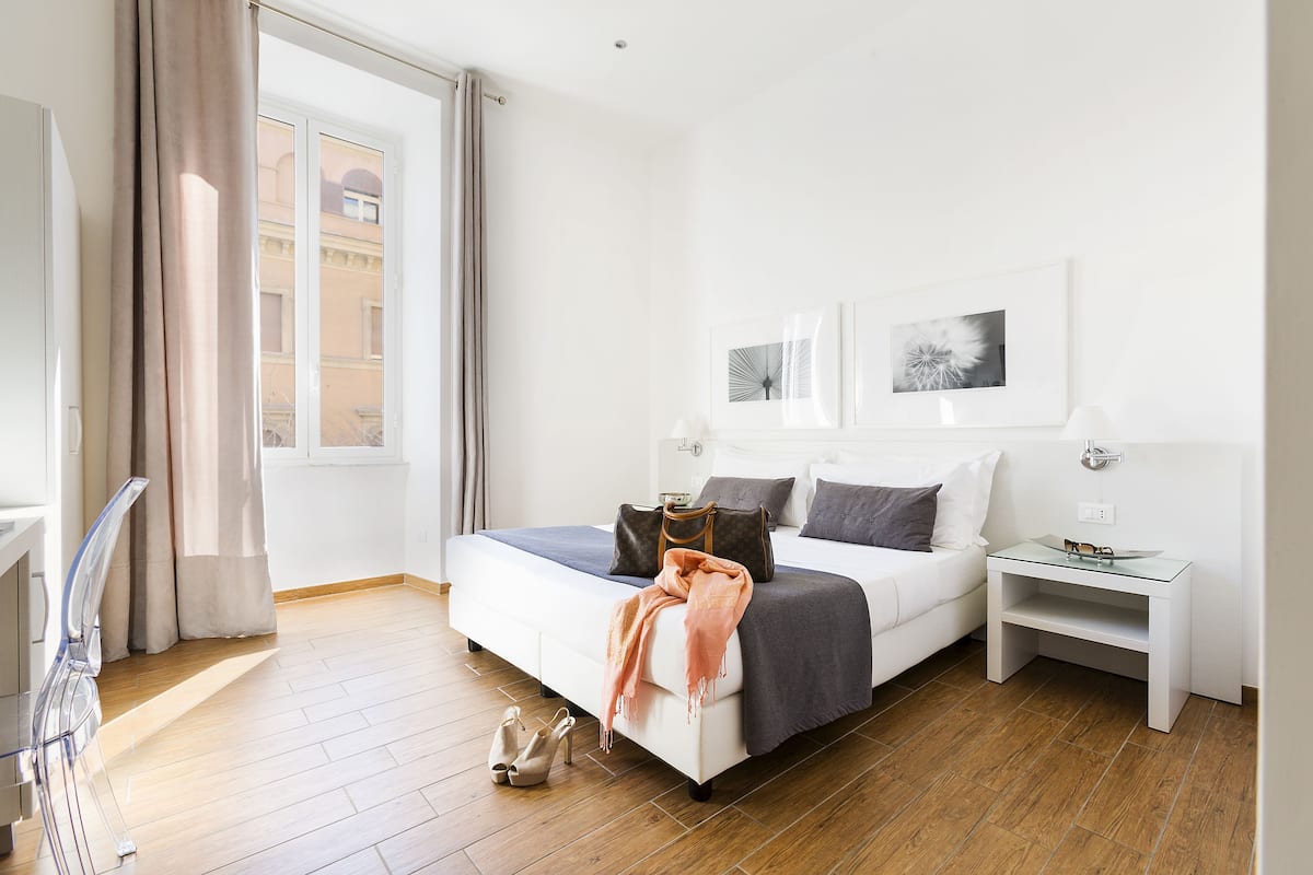 A modern hotel room with a large bed, a bedside table, and a view of the city through the window.