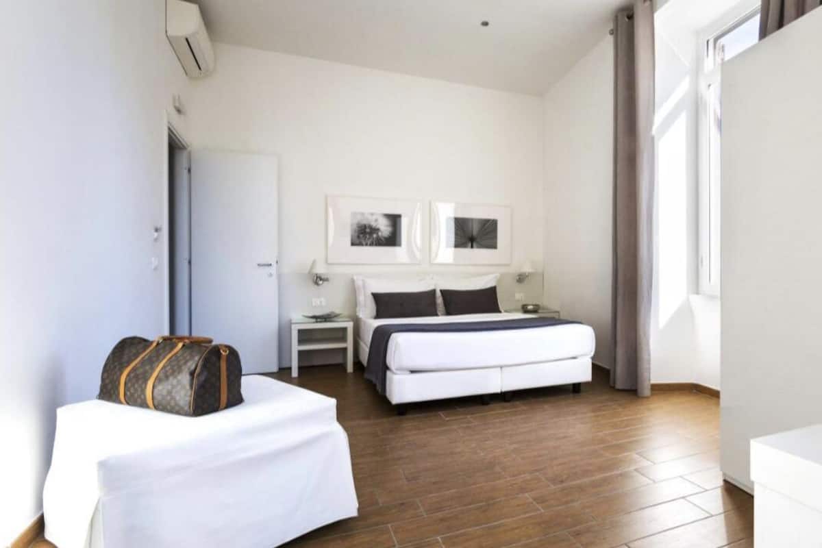 A hotel room with a bed, a bedside table, a chair, a wardrobe, and a suitcase.