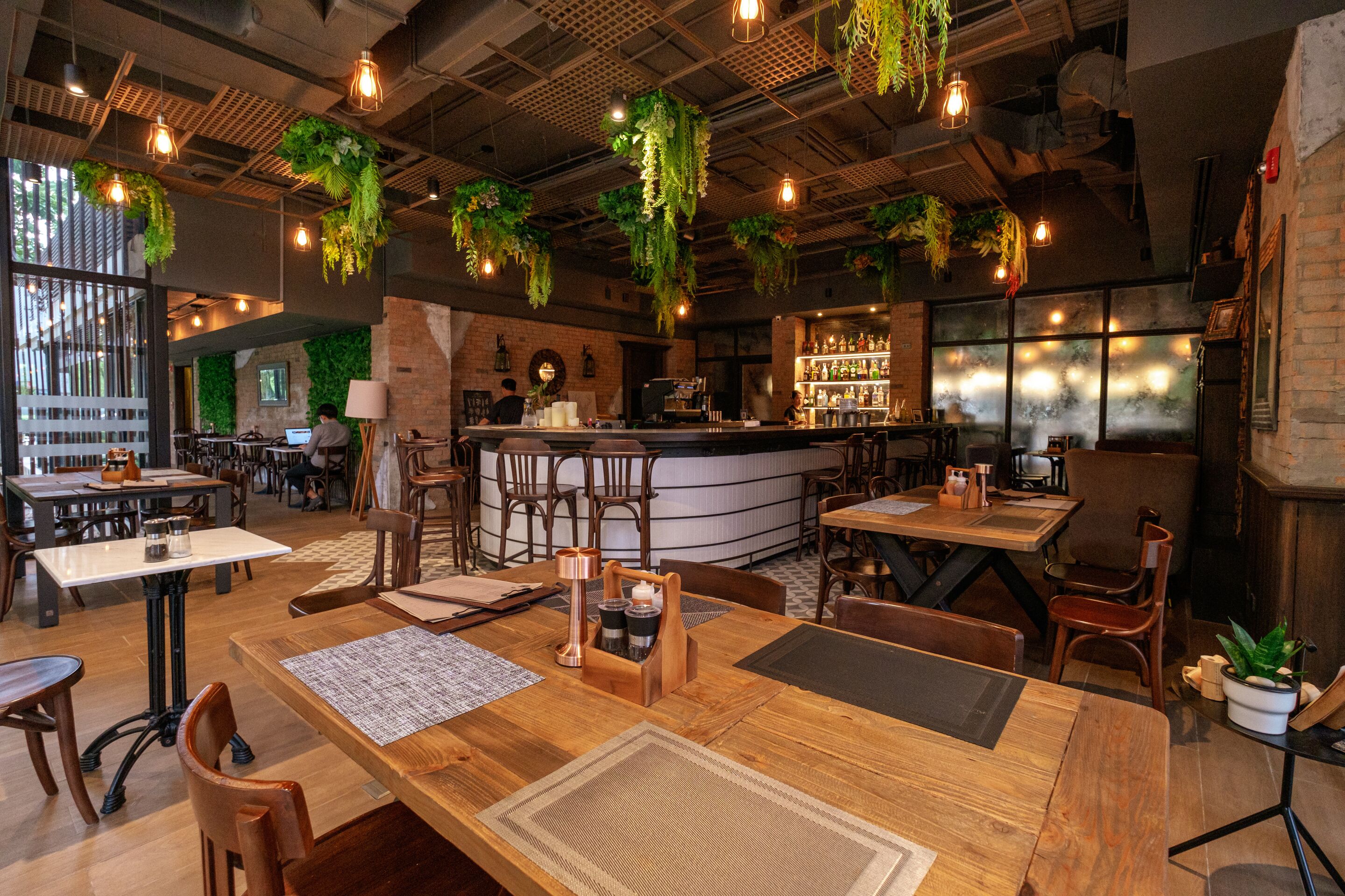 Ein Restaurant mit Holztischen, hängenden Pflanzen und einer Bar.