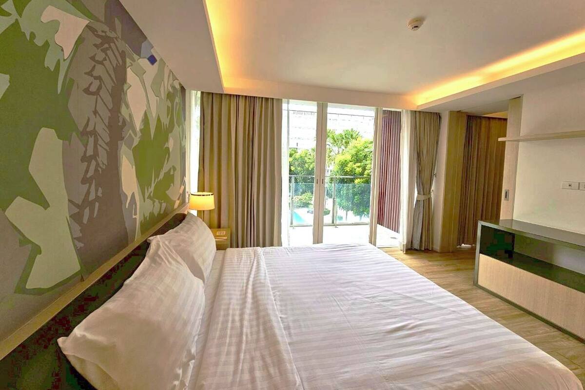 Habitació d'hotel amb un llit gran, televisió i un balcó amb cortines.