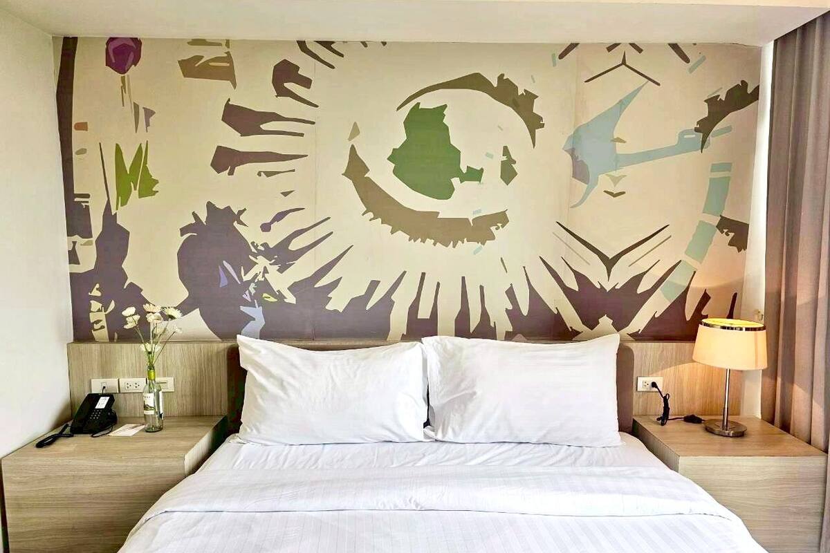 Habitació d'hotel amb un llit gran, dues taules de nit, un mural a la paret, un telèfon i una làmpada.