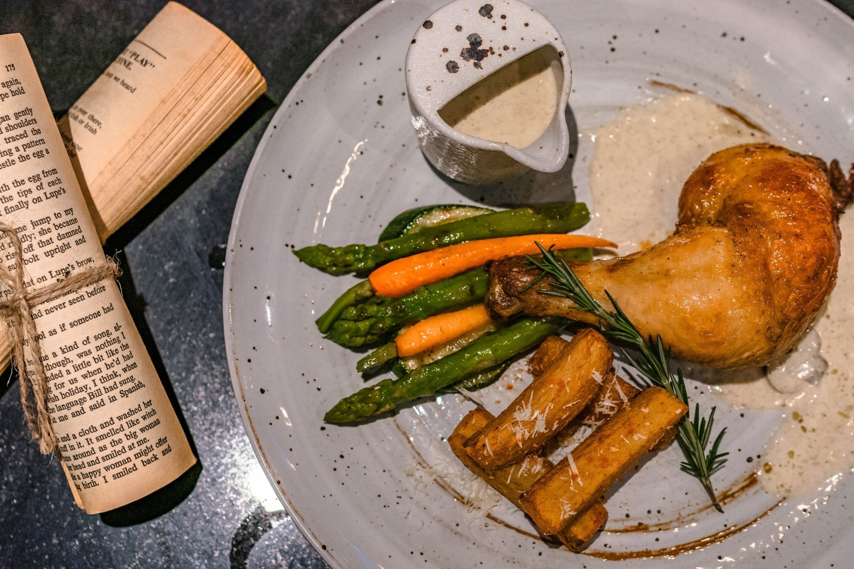 A plate with roasted chicken, asparagus, carrots, and fries, accompanied by a gravy boat.