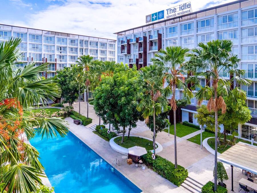 Ein modernes Hotel mit Schwimmbad, umgeben von Palmen und viel Grün.