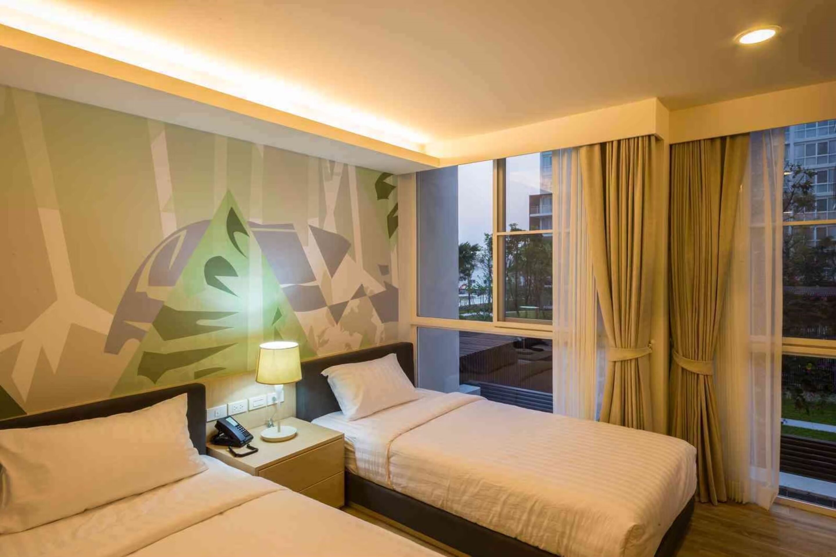 Een hotelkamer met twee bedden, een nachtkastje met een lamp, een telefoon en een muur met een geometrisch patroon.