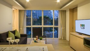 A modern living room with a large window, a sofa, a coffee table with decorative items, and a television on a stand. - The Idle Hotel and Residence (Khlong Luang)