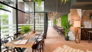 A modern restaurant with wooden tables and chairs, potted plants, and a brick wall. - The Idle Hotel and Residence (Khlong Luang)