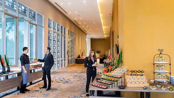 A hotel lobby with a reception desk, a buffet with various food items, and a seating area with a sofa and chairs.