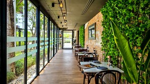 A long corridor with tables and chairs, large windows, and a brick wall with greenery. - The Idle Hotel and Residence (Khlong Luang)