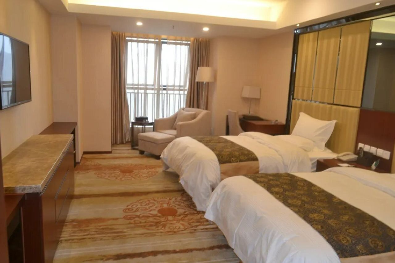 A hotel room with two beds, a desk, a chair, a TV, and a window with curtains.